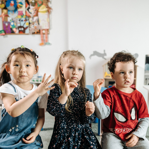Three young children make hand gestures in their school classroom, links to information on preschool readiness