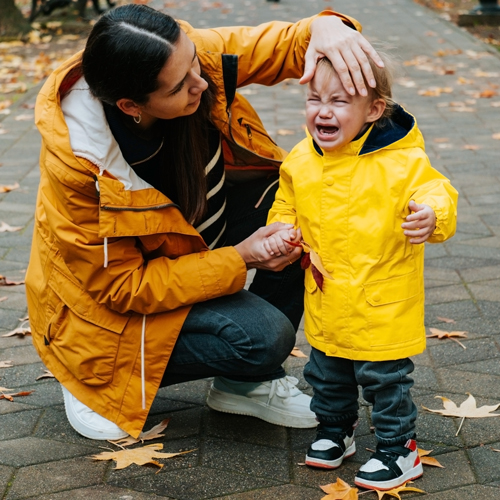 A crying young child in a rain coat is comforted by an adult, links to information on helping young children co-regulate their emotions