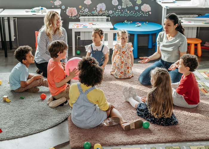 A group of young children interact with their teachers in a preschool classroom