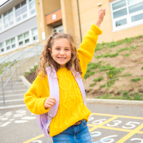 Young girl wearing a backpack smiles with one arm up in the air, links to information on self regulation.