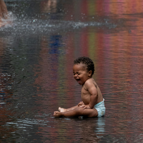 A baby laughing and having a good time while sitting in a fountain area, links to information about the benefits of playing in water for babies.