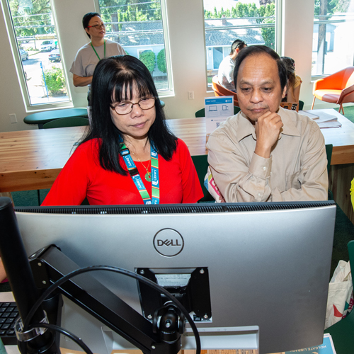  A person sits with a library staff member  in front of a computer, links to information about Digital Inclusion Week.